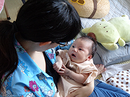 写真：和室で、手元に抱える乳児の顔を覗き込む女性