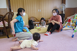 写真：2人の乳児と、床に座り会話する、別の2人の女性